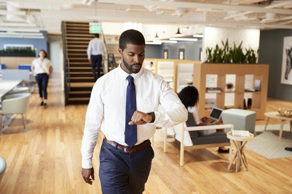 Businessman Walking Through Modern Office Checking Health Data On Smart Watch